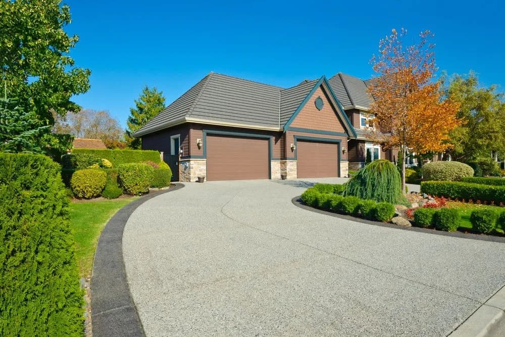 Wide exposed aggregate concrete driveway curving up to a landscaped home